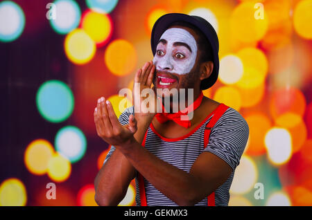 L'homme avec la peinture faciale Pantomime posant pour la tenue de l'appareil photo, de l'avertisseur sonore de soufflage lumières fond flou Banque D'Images