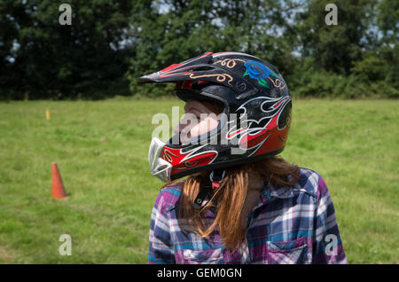 Fille aux cheveux rouges en casque de moto et chemise à rire dans un champ à la campagne Banque D'Images