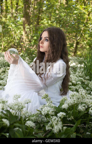 Belle jeune femme vêtue d'une robe blanche dans une forêt tenant une boule de cristal Banque D'Images