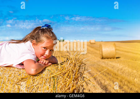 Cute young girl having fun on haystack. Des piles de paille - les balles de foin, roulé en piles à gauche après la récolte de blé, les oreilles Banque D'Images