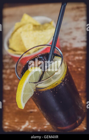 Cola contenant de verre avec du citron et un petit bol de nachos dans l'arrière-plan Banque D'Images