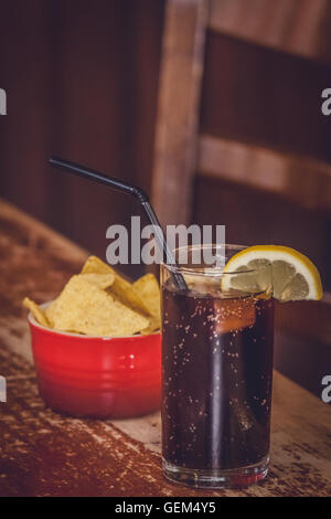 Cola contenant de verre avec du citron et un petit bol de nachos dans l'arrière-plan Banque D'Images