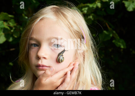 Portrait of cute blonde enfant fille avec escargot sur son visage Banque D'Images