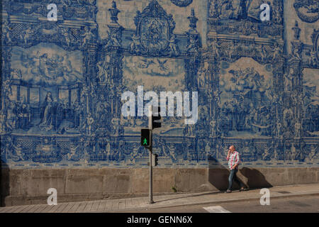 Un homme marche sous tuiles azulejo traditionnel sur le mur de Capela Das Almas (église), sur la Rua Santa Catarina Porto, Portugal. Banque D'Images