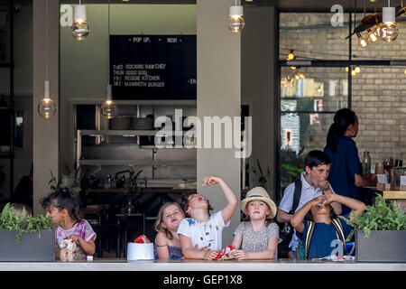 Un groupe d'enfants Les enfants bénéficient d'une collation dans un café en plein air. Banque D'Images