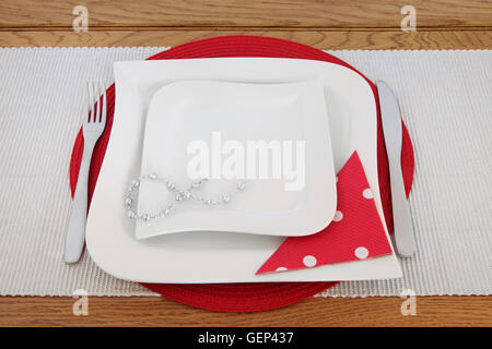 Table avec assiettes, couverts en porcelaine blanche, perles, chaîne serviette à pois rouge sur place mat. Banque D'Images