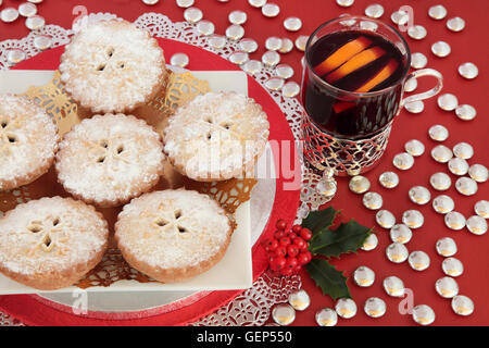 Mince pie gâteaux de Noël avec vin chaud, Holly et d'argent bouton chocolat décorations sur fond rouge. Banque D'Images