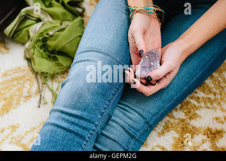 Une femme assise tenant un petit cristal violet dans ses mains. Banque D'Images