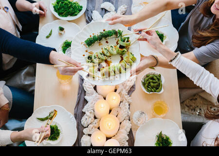 Vue de dessus de quatre personnes partageant un repas, plateaux de sushis et une table pour un repas de fête. Banque D'Images