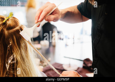 Les cheveux d'un coloriste, un homme à l'aide d'un pinceau de traiter des articles de la femme, les cheveux blonds. Banque D'Images