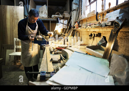 Homme debout à une table de travail dans un atelier de menuiserie, de travailler sur un morceau de bois fixé dans un étau. Banque D'Images