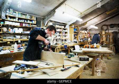 Homme debout à une table de travail dans un atelier de menuiserie, de travailler sur un morceau de bois, à l'aide d'une perceuse. Banque D'Images