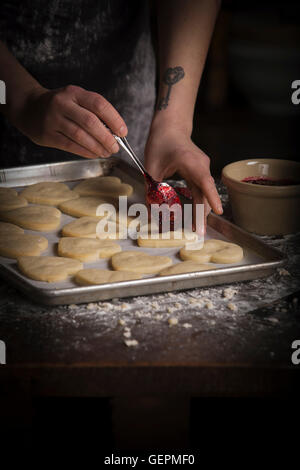 La Saint-Valentin, femme répandre la confiture de framboises sur les biscuits en forme de coeur. Banque D'Images