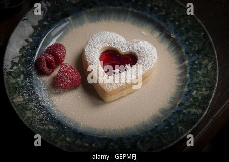 La Saint-Valentin, high angle view d'une plaque à biscuits en forme de cœur et de framboises fraîches. Banque D'Images