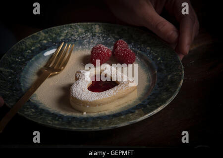 La Saint-Valentin, high angle view d'une plaque à biscuits en forme de cœur et de framboises fraîches. Banque D'Images