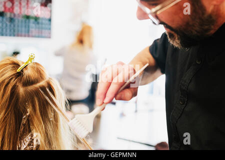 Les cheveux d'un coloriste, un homme à l'aide d'un pinceau de traiter des articles de la femme, les cheveux blonds. Banque D'Images