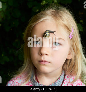 Portrait of cute blonde enfant fille avec escargot sur son visage Banque D'Images