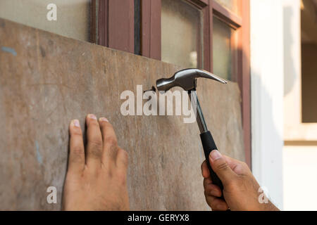 Hammer arrivera le clou par l'homme pour la fenêtre de séquence avec la plaque de bois Banque D'Images