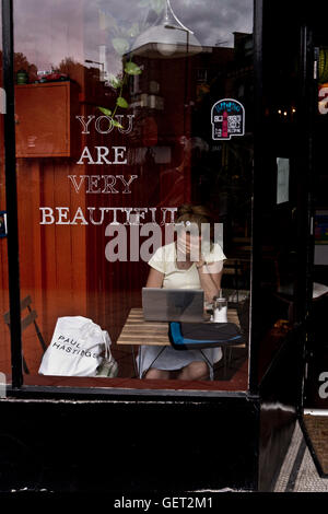 Une femme cache son visage avec sa main alors qu'elle travaille sur son ordinateur portable dans un café de Londres. Banque D'Images