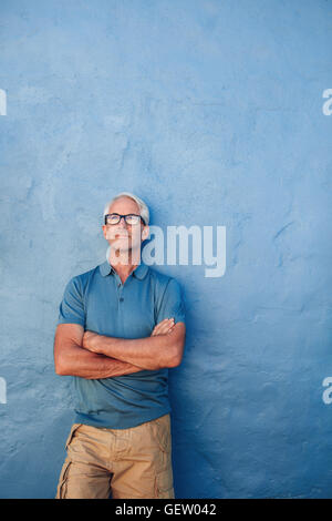 Portrait of young man standing sur un fond bleu. Beau mâle dans les verres debout avec les bras croisés un Banque D'Images