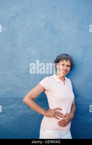 Portrait of attractive young woman posing à huis clos contre fond bleu. Les femmes d'âge moyen standing avec ses mains sur les hanches Banque D'Images