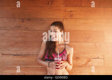 Portrait of young woman avec verre de jus de fruit sur fond de bois. Modèle des femmes de race blanche dans les vêtements de sport avec jui Banque D'Images