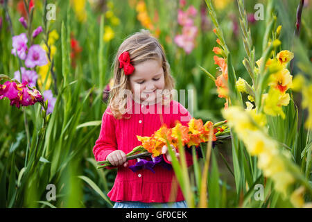 Little girl holding glaïeul fleurs''. Préparation de l'enfant des fleurs fraîches dans le jardin. Jardinage Enfants en automne Banque D'Images