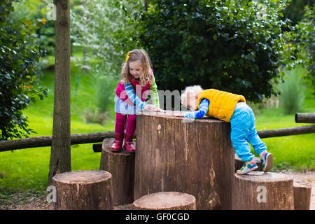 Petit garçon et fille d'escalade sur une aire de jeux en bois dans un parc. Les enfants jouer dehors par une froide journée d'automne. Banque D'Images