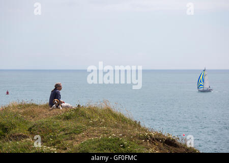 Femme et chien assis au point de Peveril yacht avec passant par dans la distance, Swanage, Dorset en Juillet Banque D'Images