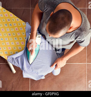 Capture d'un grand angle d'un jeune homme planche une chemise rayée avec un fer électrique sur une planche à repasser Banque D'Images