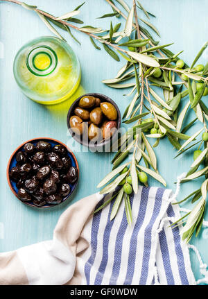 Deux bols avec olives vertes et noires marinées, olive tree branches fraîches maison, l'huile sur fond turquoise bleu Banque D'Images