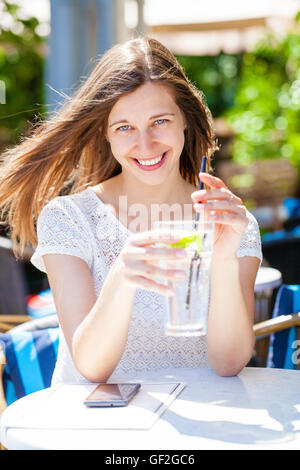 Belle jeune femme brune avec une boisson froide assis dans un café sur la rue Banque D'Images