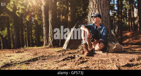 Portrait of senior man sitting par un arbre avec une tente dans l'arrière-plan. Homme mûr assis à un camping. Banque D'Images