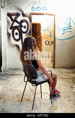 Jeune femme assise sur une chaise de bureau dans un couloir d'un hôpital psychiatrique abandonné avec Passe-partout écrits sur les murs Banque D'Images