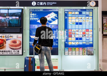 Le Japon, l'aéroport de Kansai, KIX. L'intérieur du terminal. La salle d'enregistrement. Asian man with suitcase lecture Deuxième étage information aéroport carte. Banque D'Images
