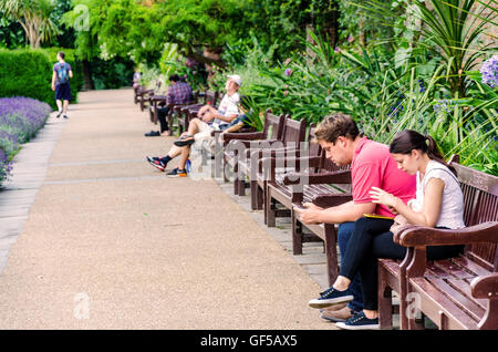 Une rangée de bancs dans Holland Park, les gens s'utiliser leur smartphone. Banque D'Images