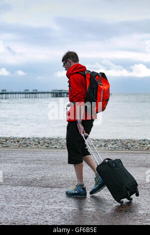 Un homme marche le long de la promenade tirant son assurance que la pluie s'abat au Llandudno, au Pays de Galles, Royaume-Uni Banque D'Images