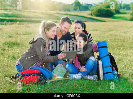 Les randonneurs du groupe sur l'herbe avec sac à dos utilisé tablet pc, en plein air d'été. Aventure, Voyage, tourisme, randonnée pédestre et personnes concept. Banque D'Images