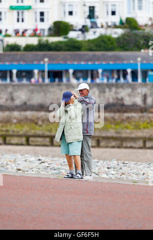 Vieux couple réglage de la couronne comme le vent se lève sur la promenade de Llandudno, au Pays de Galles, Royaume-Uni Banque D'Images