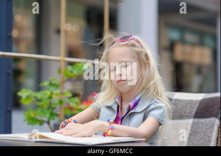 Adorable enfant menu lecture dans un café. Fatigué des tout-petits en fille magnifique à l'extérieur choix de café repas menu Carte. Banque D'Images