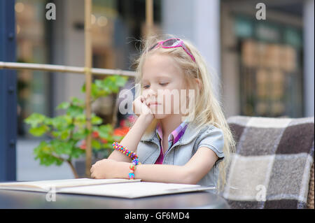 Adorable enfant menu lecture dans un café. Fatigué des tout-petits en fille magnifique à l'extérieur choix de café repas menu Carte. Banque D'Images