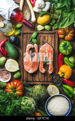 Ingrédients de cuisine le dîner. Deux morceaux de saumon cru poisson avec légumes frais, riz, herbes, citron, épices, vin rose sur planche de bois rustique, vue du dessus Banque D'Images