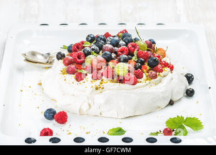 Des Pavlova gâteau avec jardin frais et baies sauvages sur plaque blanche sur fond de bois clair Banque D'Images