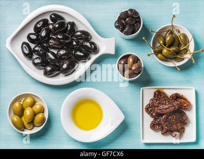 Snack-méditerranéen assortiment. Noir et vert Greek olives, câpres, huile d'olive, tomates séchées au soleil sur fond bleu turquoise Banque D'Images