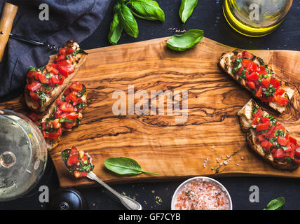 Bruschetta Tomate et basilic avec verre de vin blanc sur la planche de bois d'olive sur fond noir Banque D'Images