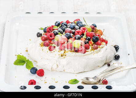 Des Pavlova gâteau avec jardin frais et baies sauvages sur blanc cuisson sur toile de lumière Banque D'Images