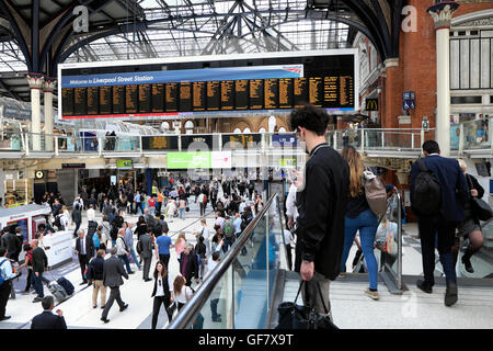 Jeune homme en regardant son téléphone portable iphone dans la gare ferroviaire de Liverpool Street, les gens sur la carte d'affichage Hall London UK KATHY DEWITT Banque D'Images