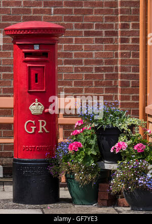 Old fashioned red poster fort utilisé dans le règne du roi George VI à côté de paniers suspendus avec des fleurs au centre ferroviaire de Didcot Banque D'Images