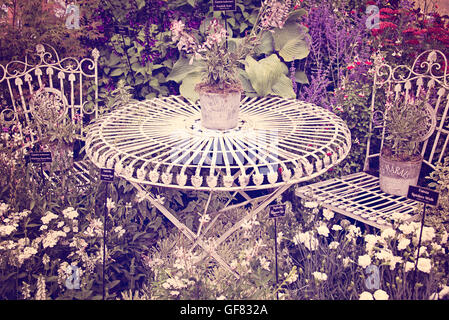 Shabby chic vintage metal mobilier de jardin table et chaises entourée de fleurs Hampton Court Flower Show à Surrey, en Angleterre. Banque D'Images