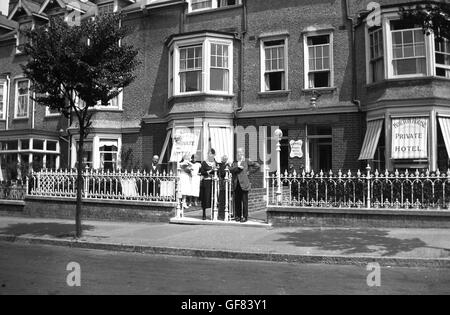 Années 1930, historique, à l'extérieur d'une rangée de maisons en terrasse victorienne, plusieurs invités se tenant à l'entrée de Norton House, un hôtel privé et géré ou pension dans une rue urbaine, Angleterre. Banque D'Images